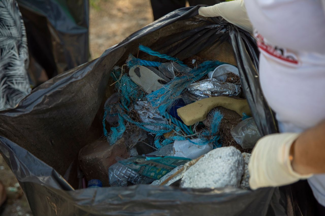 Services A close-up shot of a black trash bag filled with assorted garbage, including plastic waste.