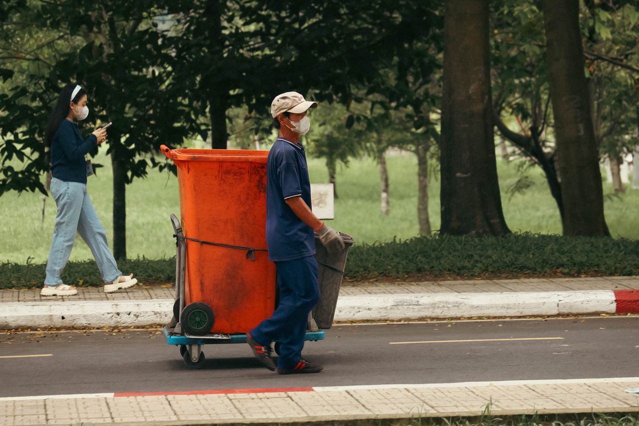 Services A waste worker pushing a bin cart on a city street while a pedestrian walks by.